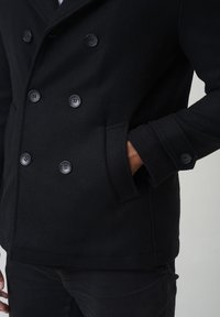 Schwarzer doppelt knöpfbarer Peacoat mit großen Knöpfen, einem strukturierten Stoff und seitlichen Taschen, ausgestattet mit einem klassischen Kragendesign.