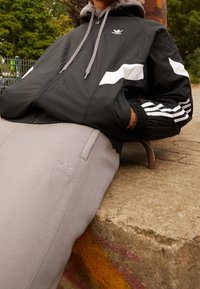 Svart vindjacka med vita detaljer, grå hoodie under, parat med ljusgrå sweatpants med logobroderi.