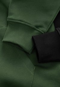 Vihreä ja musta collegepaita, jossa on ribbaudet, sileä pinta ja kontrastivärit, jotka korostavat ompelutaituruutta.
