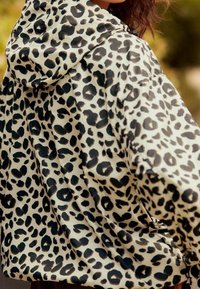 Vrouw in een gevoerde jas met een wit en zwart luipaard printpatroon, van achteren en iets opzij gekeerd.