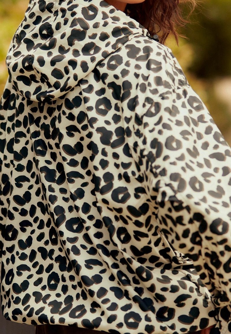 Vrouw in een gevoerde jas met een wit en zwart luipaard printpatroon, van achteren en iets opzij gekeerd.