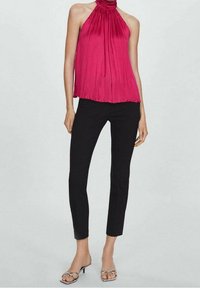 Top halter a pieghe magenta abbinato a pantaloni neri slim e tacchi trasparenti con cinturini. Texture liscia, vestibilità ampia, design senza maniche.