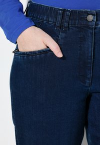 Ciemnoniebieskie dżinsy denimowe o gładkiej fakturze, zwężanym kroju i detalach kieszeni przednich, zestawione z długim, niebieskim topem.