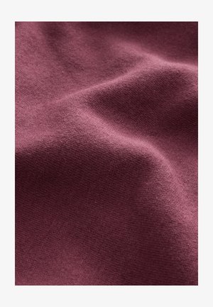 Tekstilstof i vinrød farve med en blød, glat tekstur, let elastisk og med strikkemønster. Ideel til tøj eller polstring.