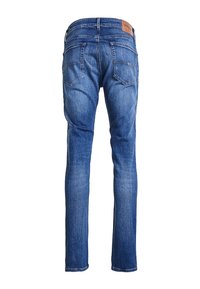 Kapeat siniset farkut, joissa on haalistunut pinta, viisi taskua ja ruskea nahkalaatta vyötäröllä, voimakkaasti kontrastoivalla ompelulla.