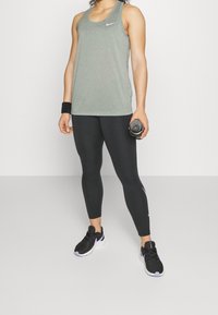 Šedý sportovní top na ramínka, černé legíny, černé běžecké boty s fialovými akcenty a náramek; drží lahev s vodou.