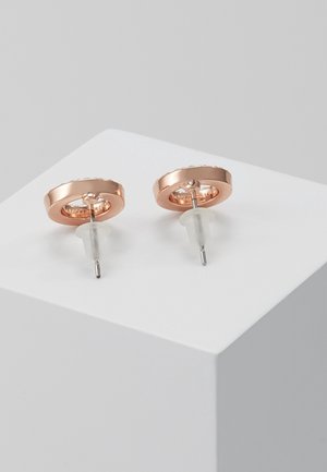 Paire de boucles d'oreilles clous circulaires en or rose avec tiges en argent et attaches transparentes, présentées sur une surface blanche.
