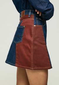 Jeanskjol med en kontrasterande blå och burgundifärgskala, med synlig sömnad och en sidoficka som extra detalj.