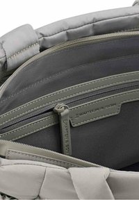 Interno di una borsa in tessuto grigio con molteplici scomparti. Presenta un bordo morbido e trapuntato e una tasca con cerniera grigia scura. Design minimalista.