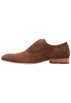 Chaussure oxford en daim marron pour homme avec laçage fermé, petit talon empilé en bois et bout pointu, vue de côté sur fond blanc.