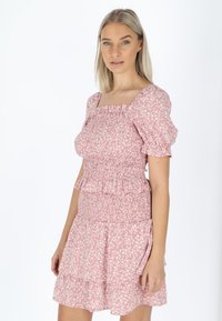 Smokket lyserødt kjole med korte puffærmer, blomstertryk, lagdelte volanger ved kanten og firkantet udskæring. Letvægtsstof, feminint design.