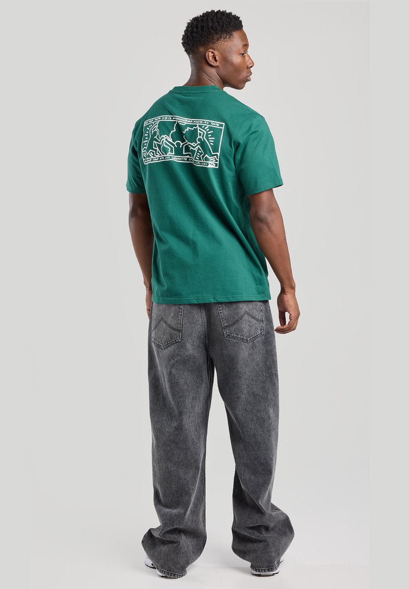 Green cotton t-shirt with a white graphic design on the back, paired with loose gray denim jeans featuring a faded texture and back pockets.