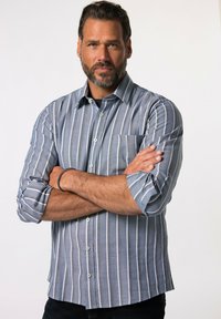 Camisa de manga larga abotonada en azul claro con rayas verticales blancas. Presenta un bolsillo en el pecho y mangas enrollables. Textura de tela suave.