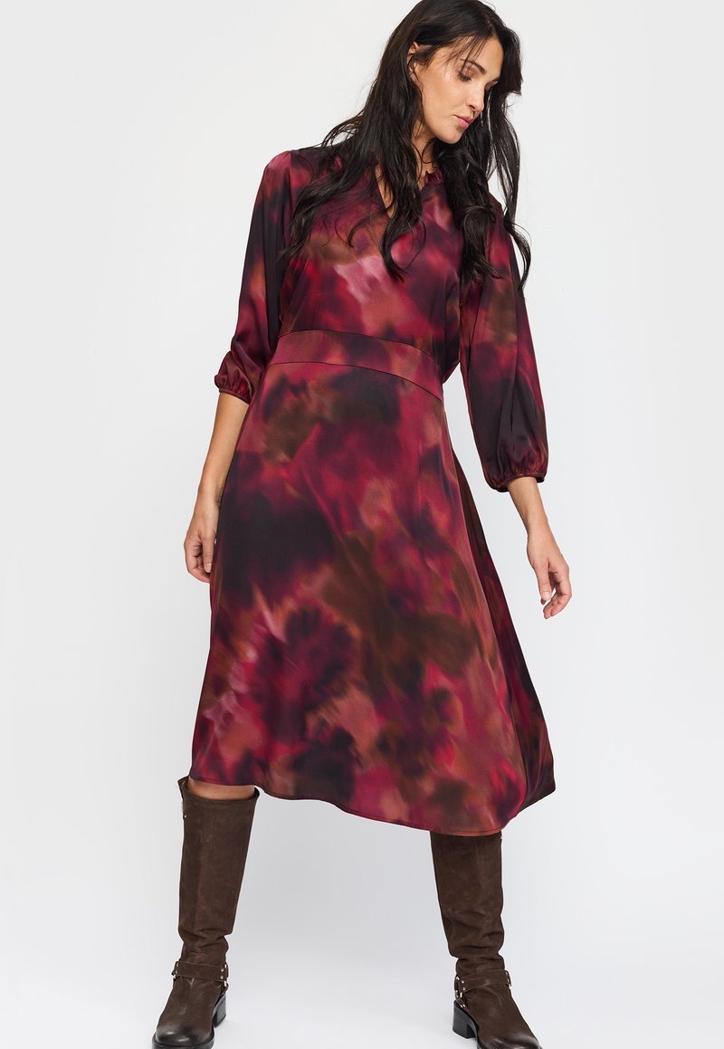 Langermet kjole i et flytende stoff med et rødt og brunt abstrakt mønster. Kne-lang design med en tettsittende midje og blafrende ermer.