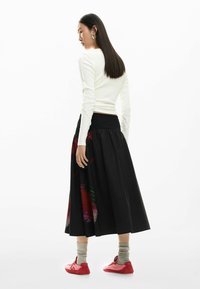 Valge pika varrukaga pluus, mida on sobitatud musta, lehvikujulise seelikuga, millel on värvikad abstraktsed mustrid, ning punased tennised hallide sokkidega.