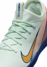 Sneaker verde chiaro con una parte superiore texture, accenti blu, swoosh dorato e lacci bianchi. Presenta un prominente etichetta "AIR ZOOM" sul tallone.