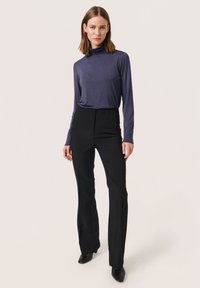 Mörkblå långärmad slim fit rullkrage i kombination med högmidjade svarta byxor, som har en slät textur och utsvängt nederkant.