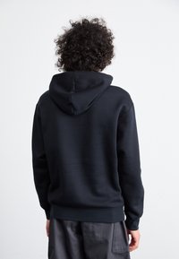 Sudadera negra con capucha de textura suave, que presenta un bolsillo tipo canguro, puños acanalados y una cinturilla, vista desde la parte de atrás.