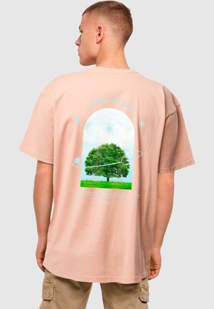 Lys rosa oversized t-shirt med et grafisk design af et træ inden for en buet ramme, med tekst og himmelske detaljer på ryggen.