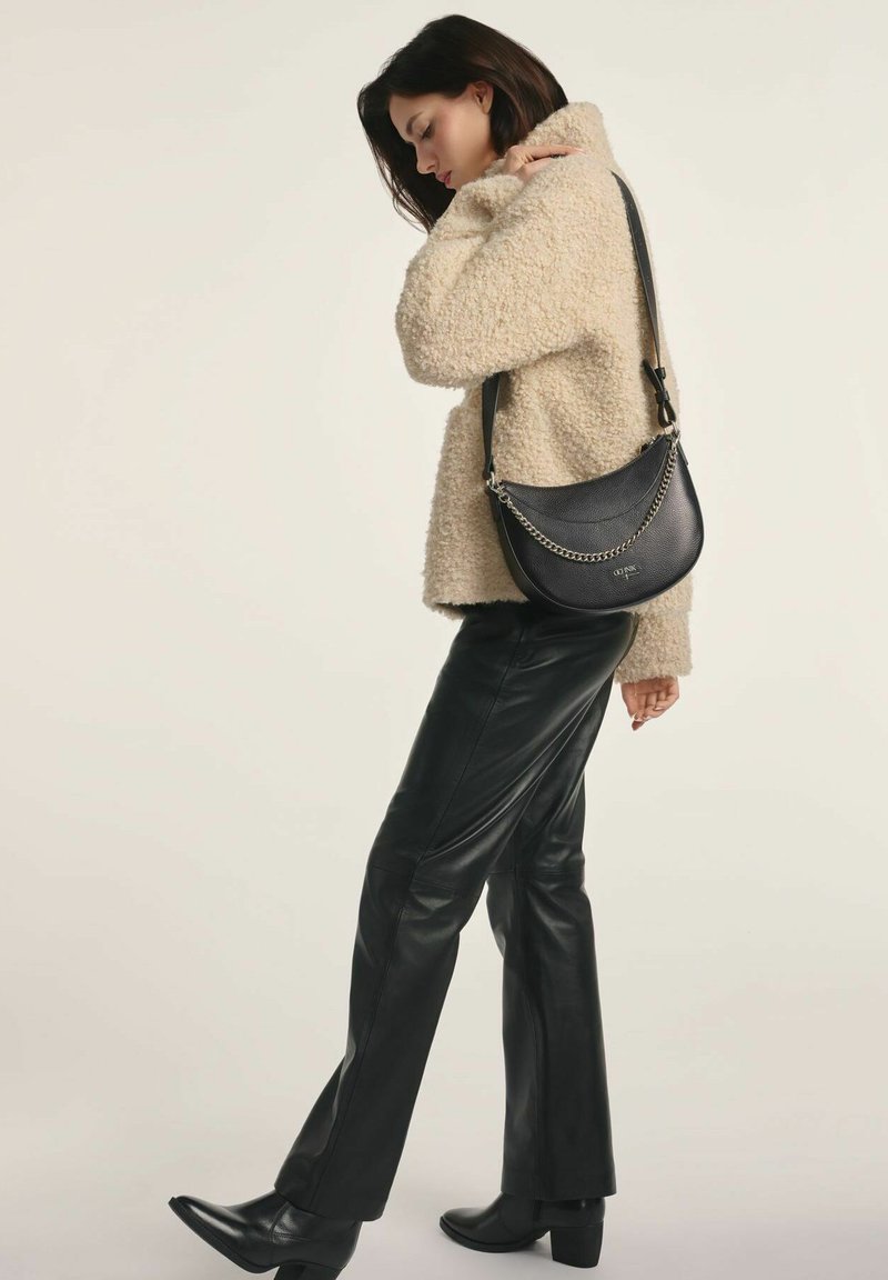Kobieta ubrana w beżową, teksturowaną kurtkę, czarne skórzane spodnie, czarne botki za kostkę oraz czarną torebkę na ramię z detalem w postaci srebrnego łańcuszka.