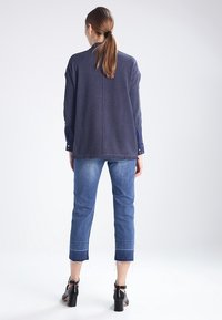 Marinblå tröja med fransad nederkant och denimjeans. Svarta klackskor. Avslappnad outfit med kontrasterande ärmar och lös passform.