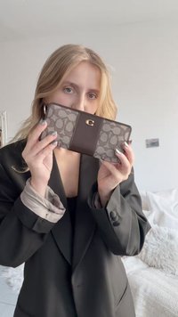 Portfel z brązowym akcentem ze skóry oraz szarą tkaniną w wzory z logo. Prostokątny kształt o gładkiej fakturze i szczegółach szwów.