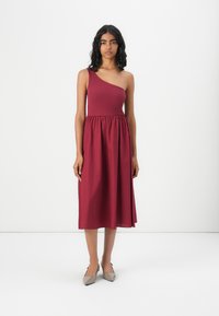 Robe bordeaux à une épaule avec un corsage ajusté et une jupe évasée. Texture lisse, longueur genou, associée à des ballerines grises pointues.