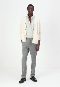 Cárdigan texturizado gris claro con botones, camisa de cuadros debajo, pantalones grises ajustados y zapatos negros. Un conjunto simple y estructurado.