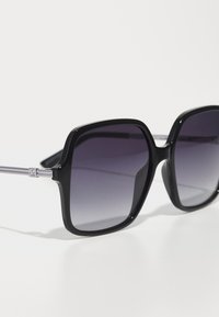 Ochelari de soare pătrați negri cu lentile întunecate cu gradient, cadru din plastic lucios și accente din metal pe tâmple.