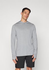 Langermet grå skjorte i lett stoff med en løs passform, med hette og subtil logo-detalj, sammen med svarte shorts.