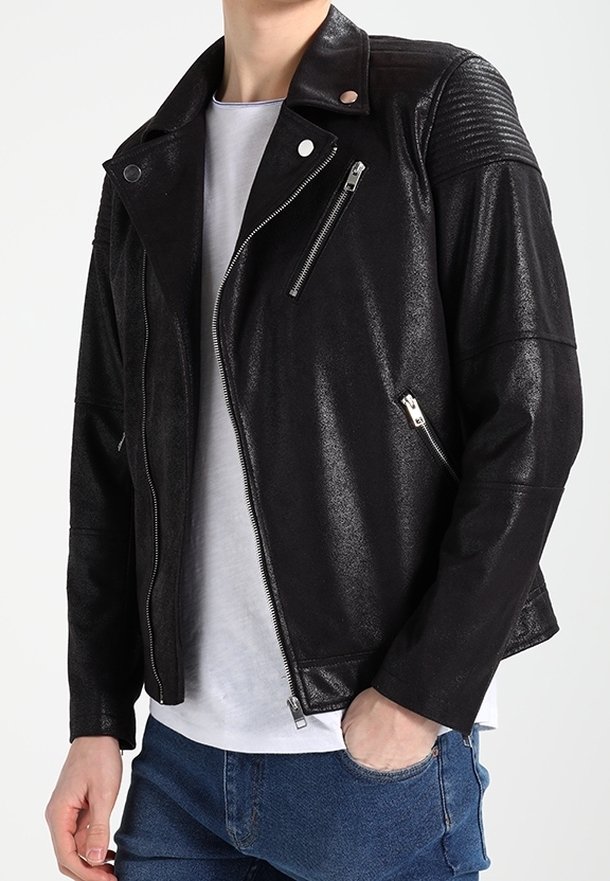 Svart fusk läder bikerjacka med dragkedjedetaljer, ribbade axelpartier och en slim fit. Bärs över en vit t-shirt och blå jeans.