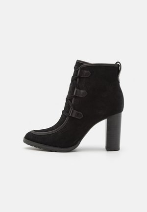 Bottine en suede noire avec un bout arrondi, un dessus texturé, des lacets décoratifs et un talon épais. Présente une bordure contrastante le long du bord.