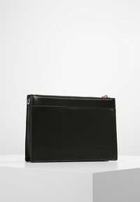 Sort læderclutch med glat tekstur, rektangulær form, lynlåslukning og hardware i guld-tone. Har et minimalistisk design med en frontlomme.