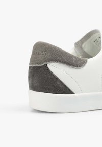 Weiße Leder-Sneaker mit grauen Wildlederakzenten, runder Form, strukturiertem Sohlenprofil und genähten Details an der Ferse.