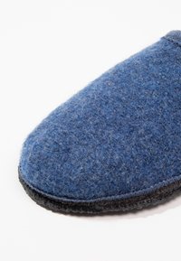 Blauwe wollen slipper met een gestructureerd oppervlak, ronde neus en een donkere rubberen zool. Naaddetail langs de rand voor duurzaamheid.