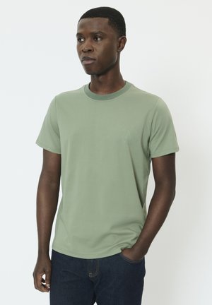 Zielony bawełniany t-shirt z okrągłym dekoltem, krótkimi rękawami i subtelnym nadrukiem na lewej piersi. W zestawie z ciemnoniebieskimi jeansami.