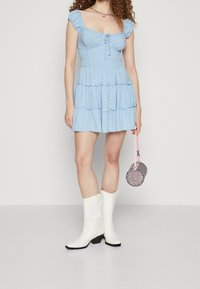 Niebieska kwiatowa mini sukienka z warstwowym dołem, krótkimi bufkami i wiązanym przodem. Noszona z białymi kowbojkami i różową torebką w kształcie okręgu z koralików.