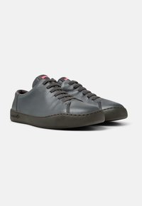 Sneakers in pelle grigia con punta arrotondata, superficie testurizzata e suola in gomma marrone. Presentano un design con lacci e un piccolo logo sulla linguetta.