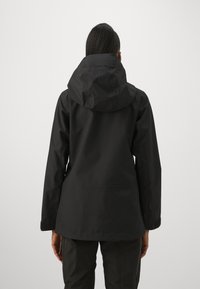 Veste imperméable noire avec capuche, présentant une coupe décontractée, une texture lisse, et sans logos ni ornements visibles.