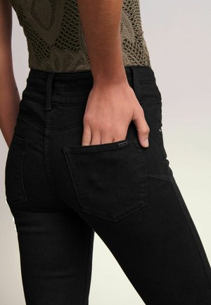 Jeans negri din denim cu un design ajustat, având un buzunar la spate, bucle pentru curea și o textură netedă. Țesătura pare flexibilă și durabilă.