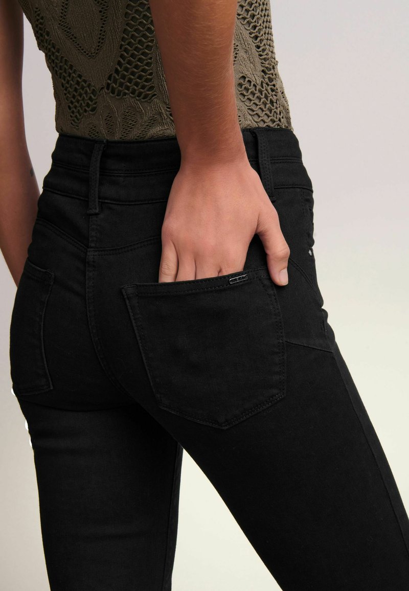 Zwarte denim jeans met een getailleerd ontwerp, voorzien van een achterzak, riemlussen en een gladde textuur. De stof lijkt flexibel en duurzaam te zijn.
