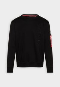 Felpa nera con scollo a girocollo, caratterizzata da un logo testurizzato sul davanti e una tasca con zip con un'etichetta rossa "RIMUOVERE PRIMA DEL VOLO".