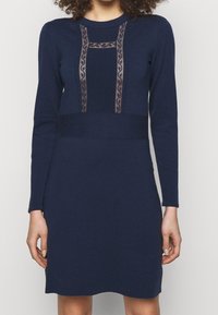 Mörkblå stickad klänning med långa ärmar, med genomskinlig mesh och ribbat detaljer på bodice, samt en åtsittande midja.