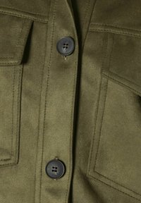 Giacca in suede verde oliva con due tasche sul petto, bottoni neri e dettagli di cucitura visibili, che mostra una finitura morbida e strutturata.