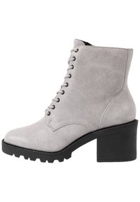 Botín de ante gris hasta el tobillo con diseño de cordones, un grueso tacón negro y suela resistente. Presenta puntera redondeada y parte superior de textura suave.