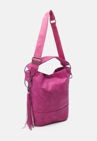 Różowa torebka z zamszu o miękkiej, teksturowanej powierzchni, z regulowanym materiałowym paskiem i dekoracyjnym akcentem w postaci skórzanej frędzla.