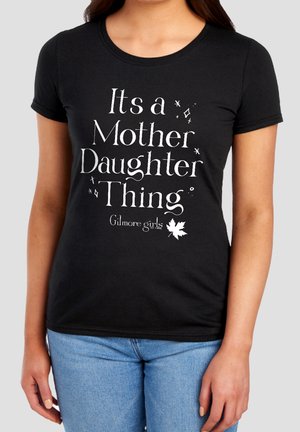 Black t-shirt worn by a person with white text saying "Its a Mother Daughter Thing" and "Gilmore girls" with a leaf graphic below.