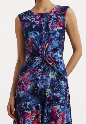 Ærmeløs kjole med blåt, lilla, rødt og gult abstrakt blomsterprint og en knudemæssig detalje i taljen, båret af en person.