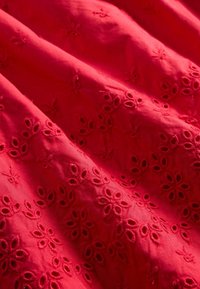 Piros szövet texturált virágos hímzéssel, apró, részletes virágmintákkal és fodros díszítéssel a sima felületen.
