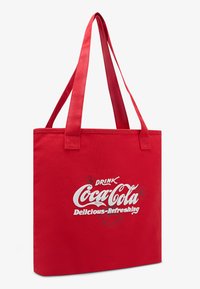 Raudona audinė maišelis su dviem rankenomis. Turėdamas baltą tekstą "GERK Coca-Cola Skani-Osviežinanti" ir vintage logotipo dizainą.